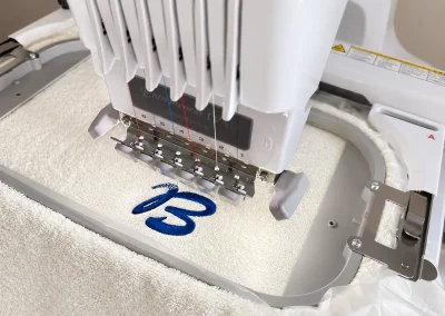 Broderie textile personnalisée en Ariège 7 Broderie d’un prénom en fil bleu sur une serviette blanche